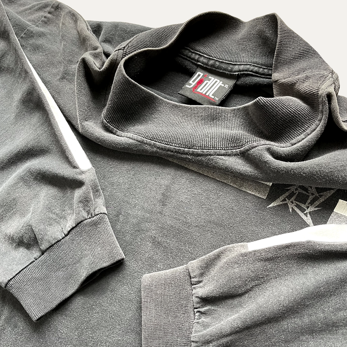 Folded gray mock neck Metallica long sleeve t-shirt with giant brand label tag on a light gray background